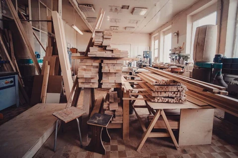 Atelier de menuiserie avec établi central supportant des planches de bois massif empilées