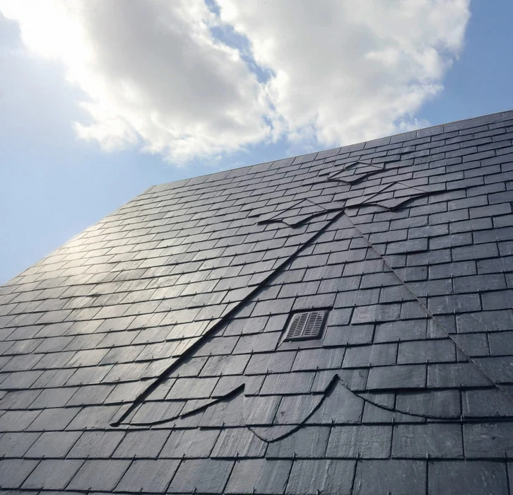 Toiture en ardoise naturelle grise vue en contre-plongée sous ciel nuageux