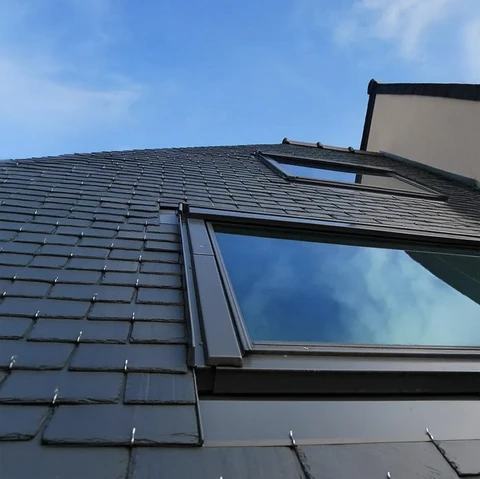 Extérieur résidentiel avec toiture en ardoises naturelles équipée de deux fenêtres de toit ouvrantes