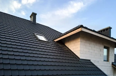 Toiture résidentielle moderne avec tuiles ardoise grises, cheminées en brique, lucarne avec fenêtre et structure murale en blocs béton