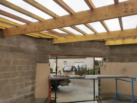 Chantier de construction résidentielle en cours, structure de maison individuelle avec murs en parpaings de béton et charpente bois apparente