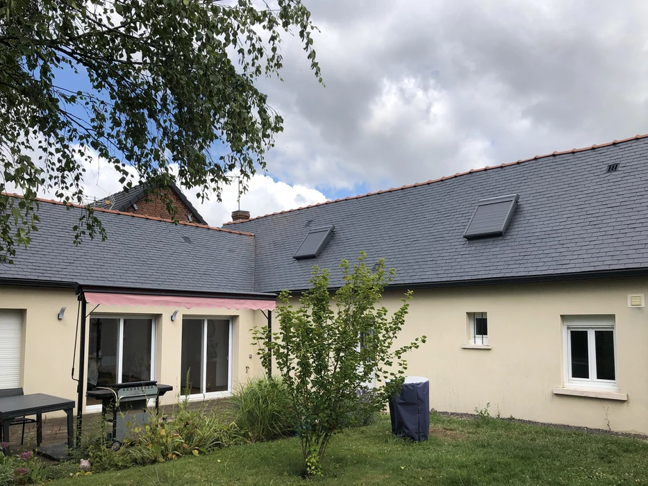 Toiture résidentielle moderne avec tuiles ardoise grises, cheminées en brique, lucarne avec fenêtre et structure murale en blocs béton