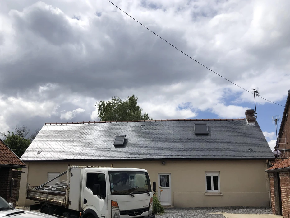 Toiture résidentielle moderne avec tuiles ardoise grises, cheminées en brique, lucarne avec fenêtre et structure murale en blocs béton