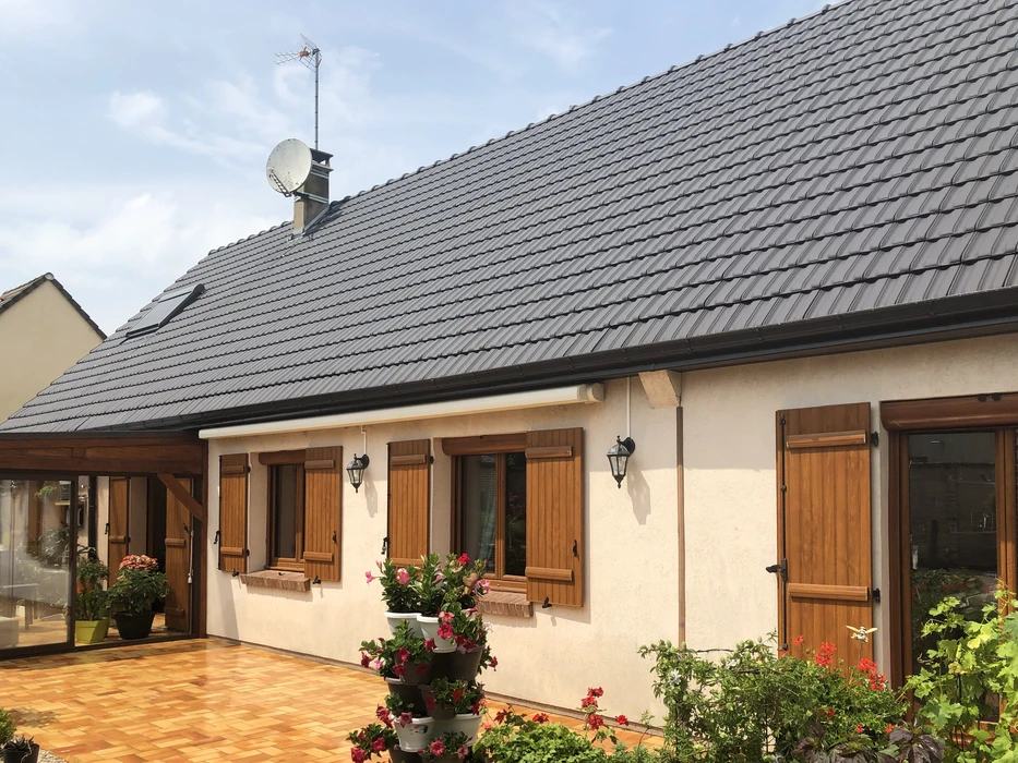 Toiture résidentielle moderne avec tuiles ardoise grises, cheminées en brique, lucarne avec fenêtre et structure murale en blocs béton